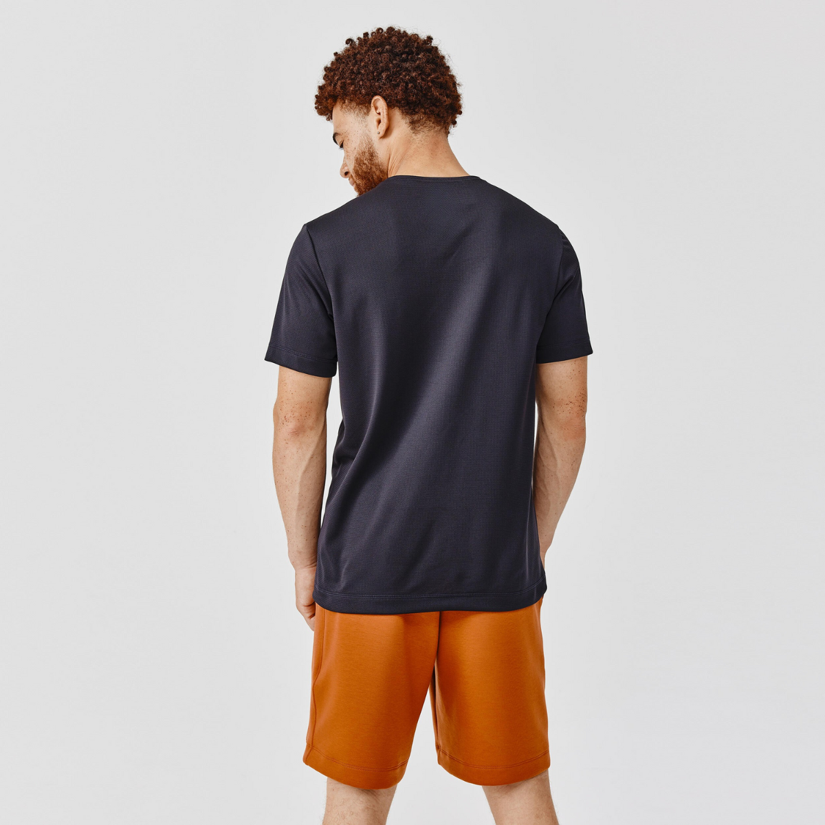 Man wearing a navy t-shirt and orange shorts on a light gray background