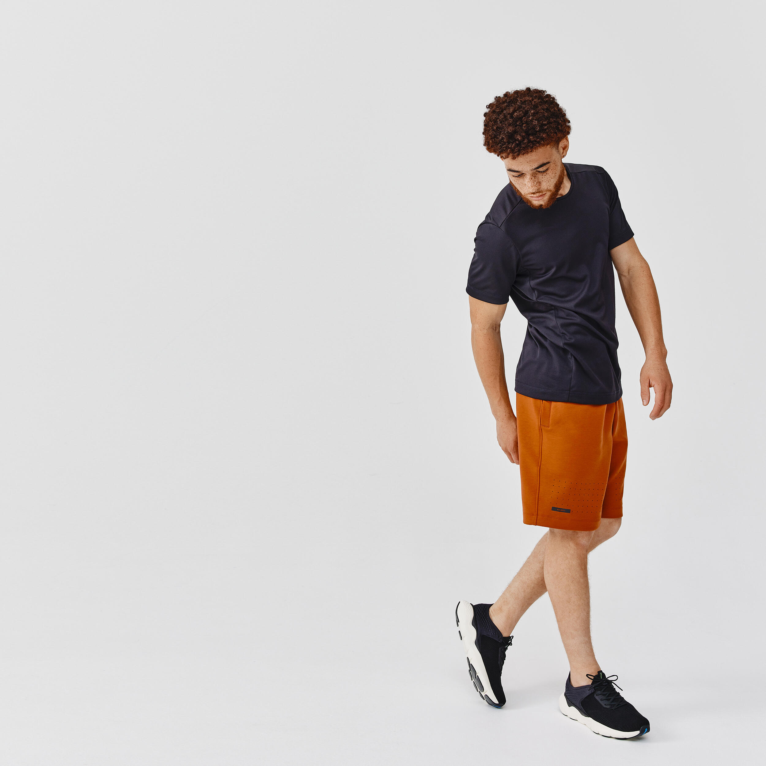 Person wearing a black t-shirt and orange shorts on a light gray background